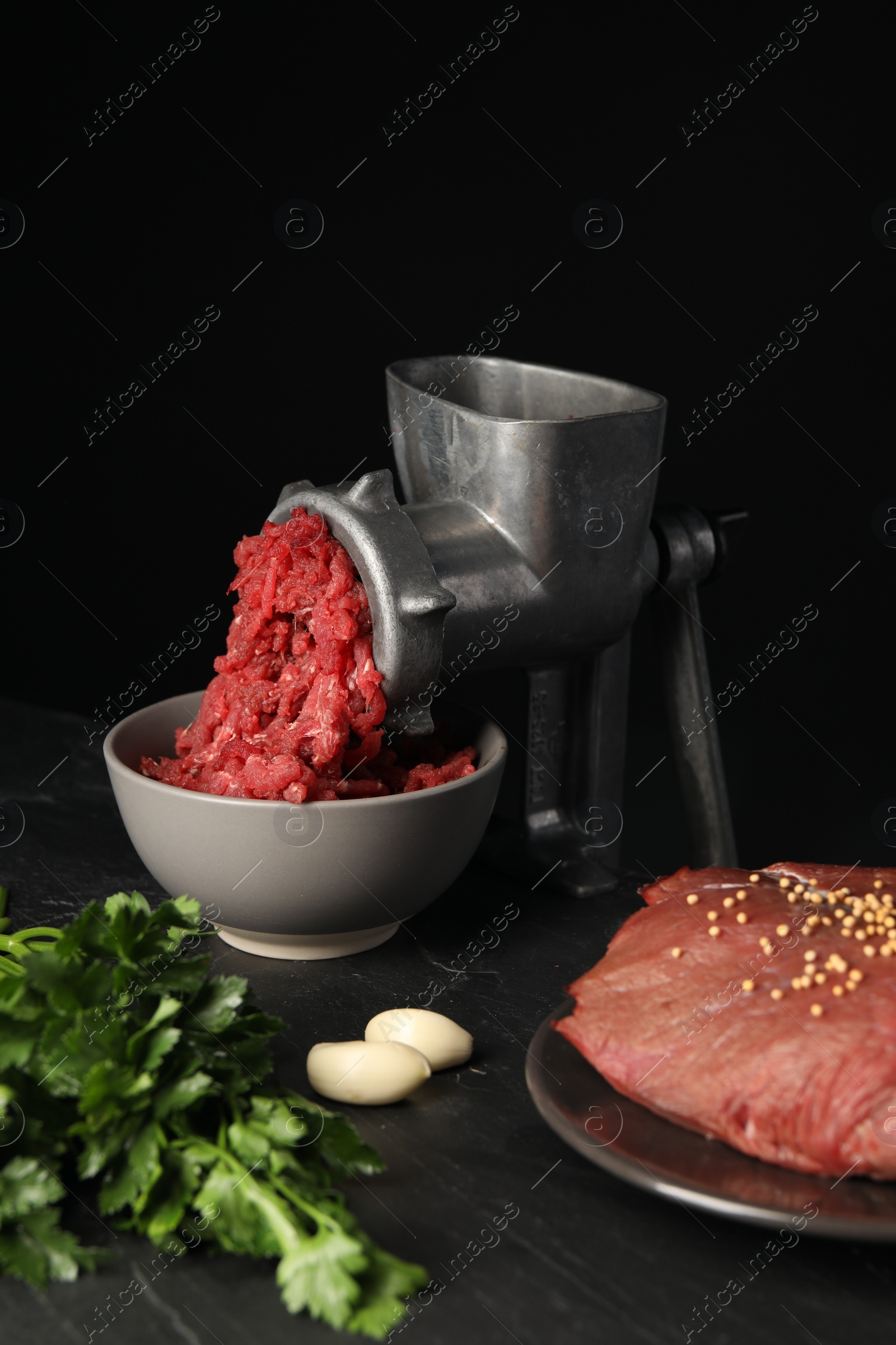 Photo of Metal meat grinder with beef mince and spices on dark textured table against black background