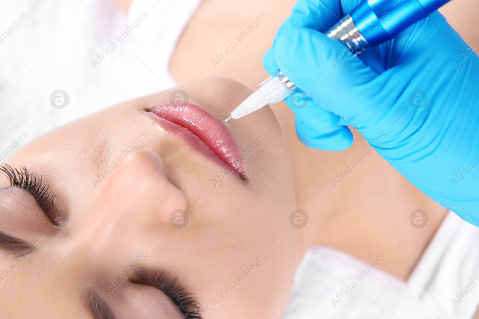 Photo of Young woman getting permanent makeup on lips in beautician salon, closeup