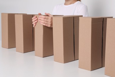 Woman folding cardboard boxes at white table, closeup. Production line