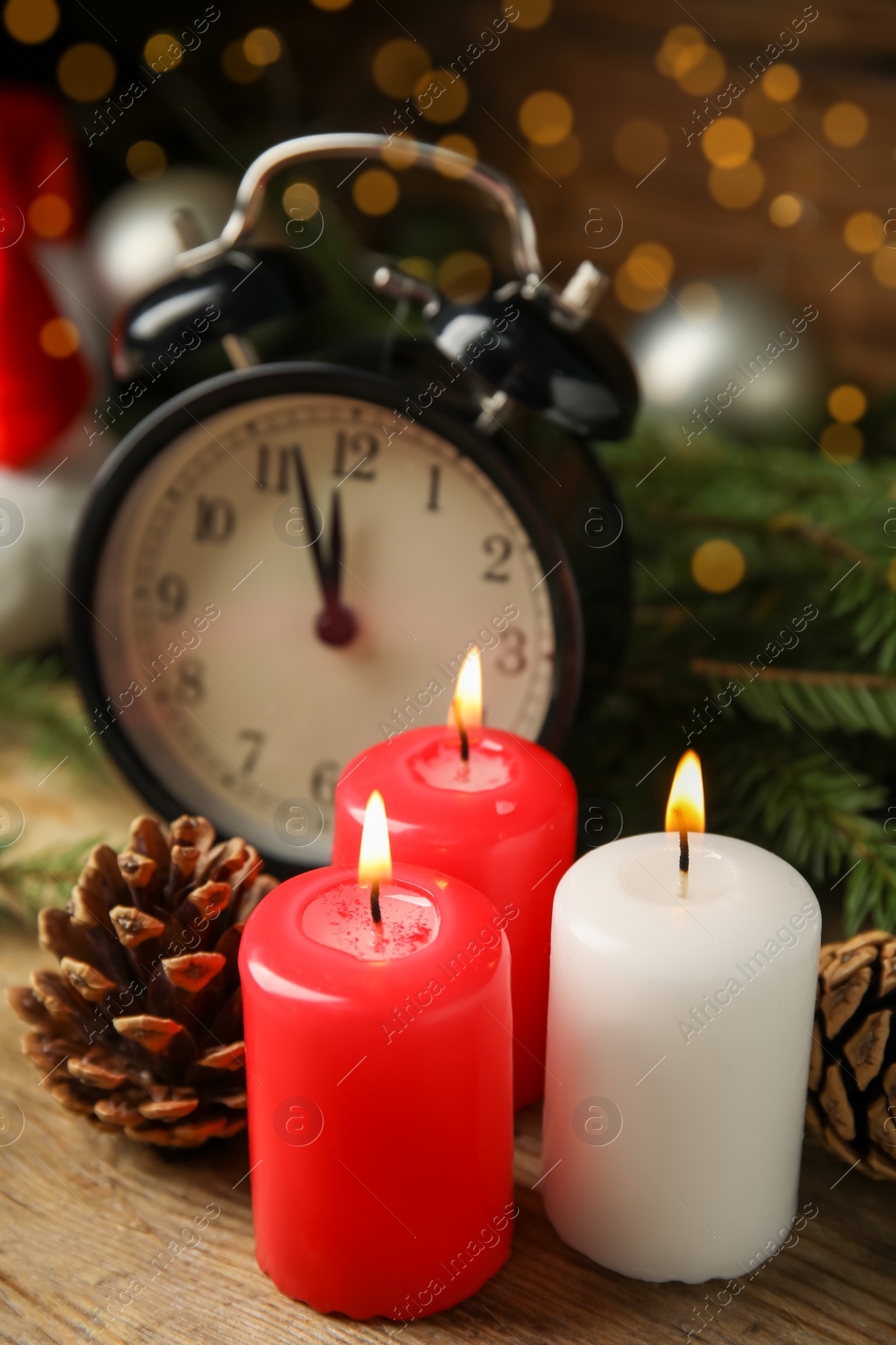 Photo of Alarm clock, burning candles and Christmas decor on wooden table, bokeh effect