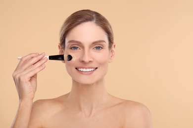 Woman applying foundation on face with brush against beige background