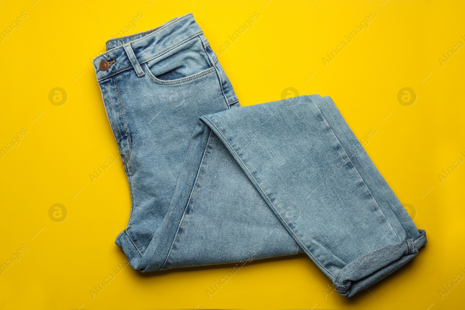 Photo of Stylish jeans on yellow background, top view