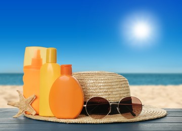 Image of Different bottles of skin sun protection products and beach accessories on blue wooden table against seascape. Space for design