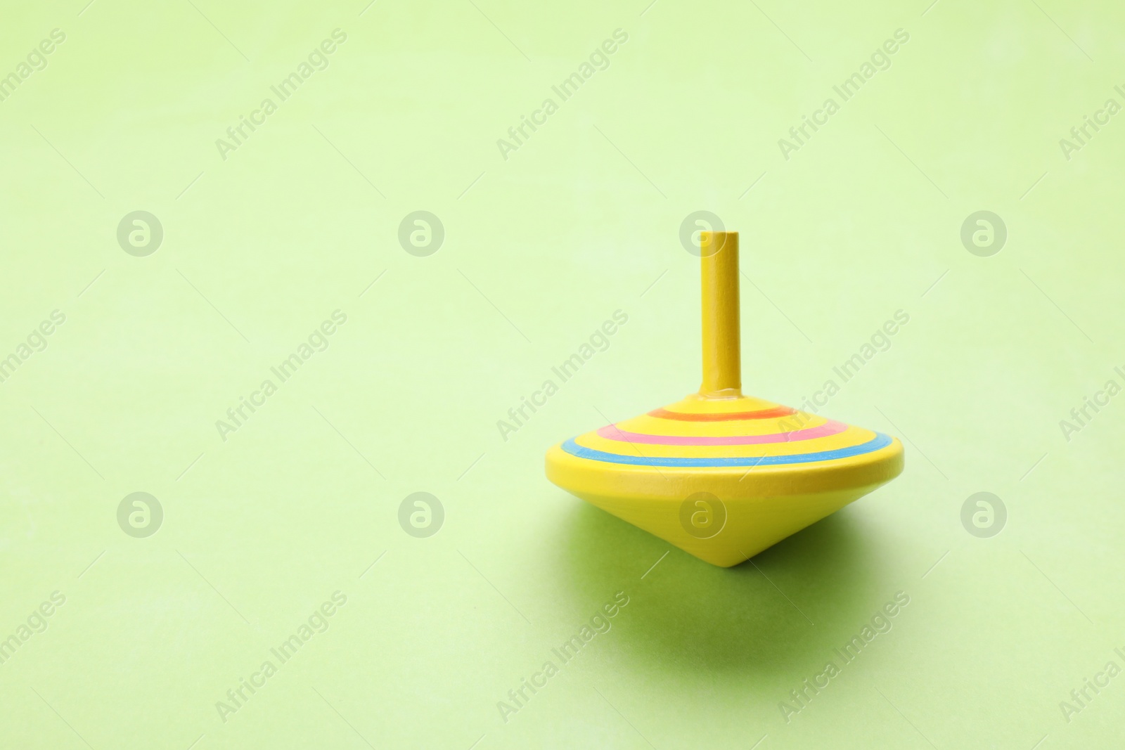Photo of One bright spinning top on light green background, space for text. Toy whirligig