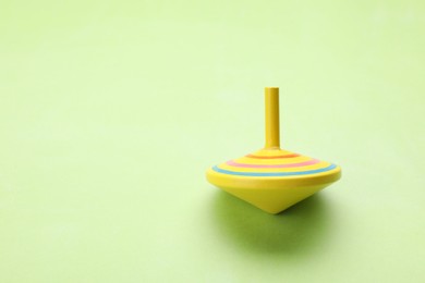 Photo of One bright spinning top on light green background, space for text. Toy whirligig