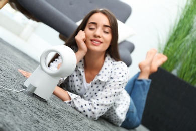 Woman enjoying air flow from portable fan at home. Summer heat