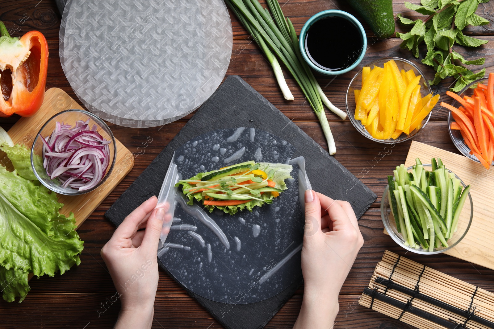 Photo of Woman making spring roll at wooden table with products, top view