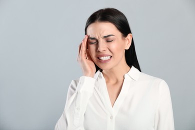 Woman suffering from migraine on grey background