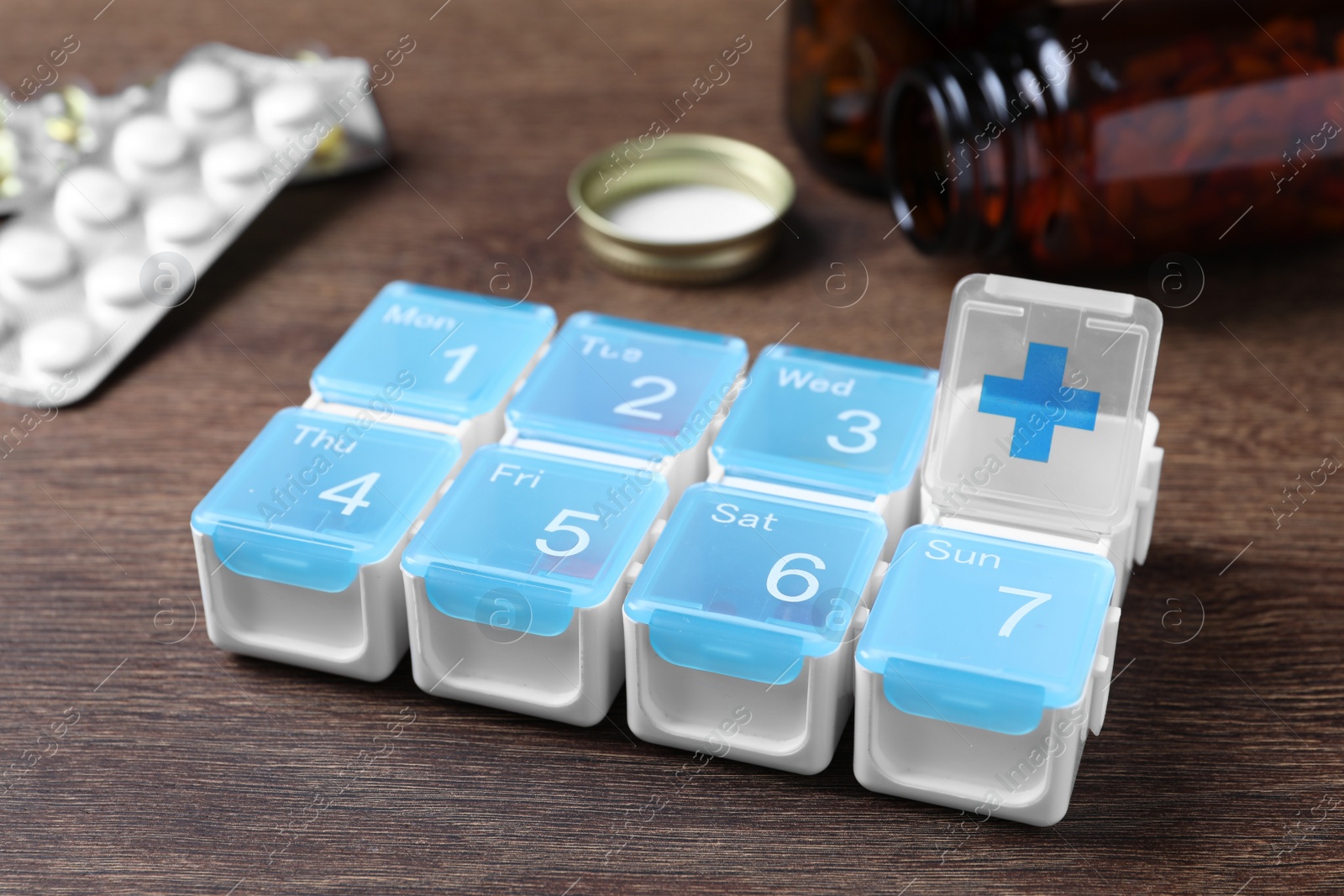 Photo of Weekly pill box with medicaments on wooden table, closeup