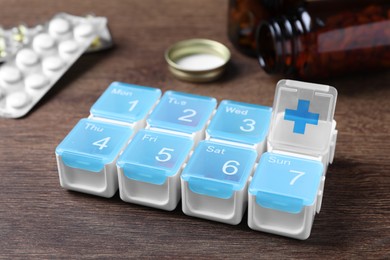 Weekly pill box with medicaments on wooden table, closeup