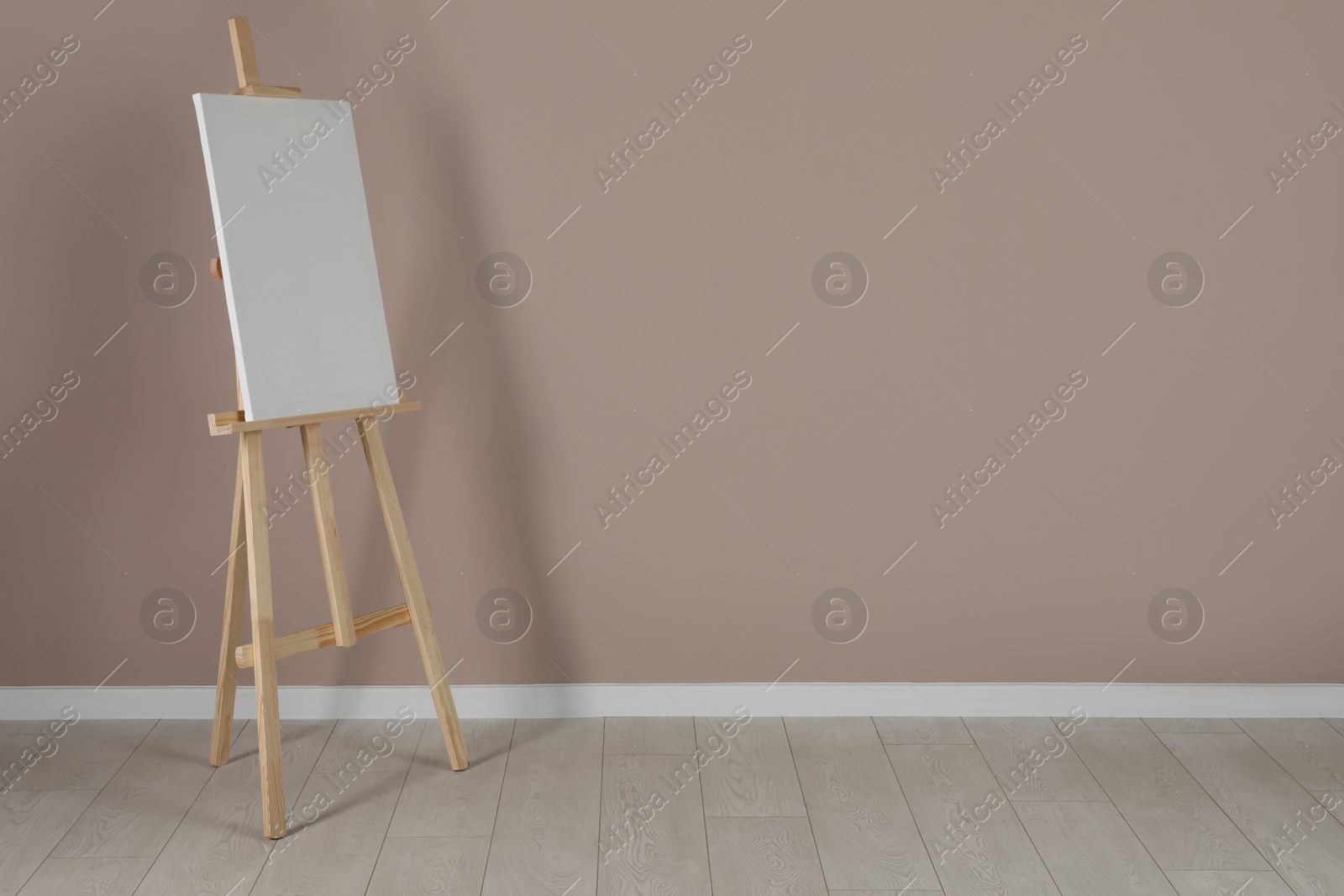 Photo of Wooden easel with blank canvas near beige wall. Space for text