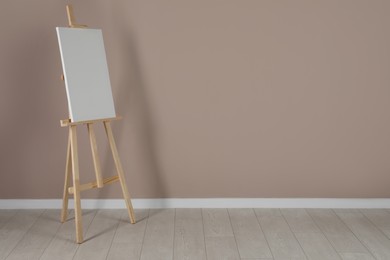 Photo of Wooden easel with blank canvas near beige wall. Space for text