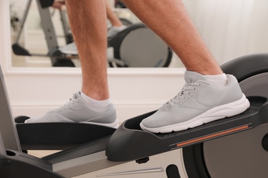 Photo of Man using modern elliptical machine indoors, closeup