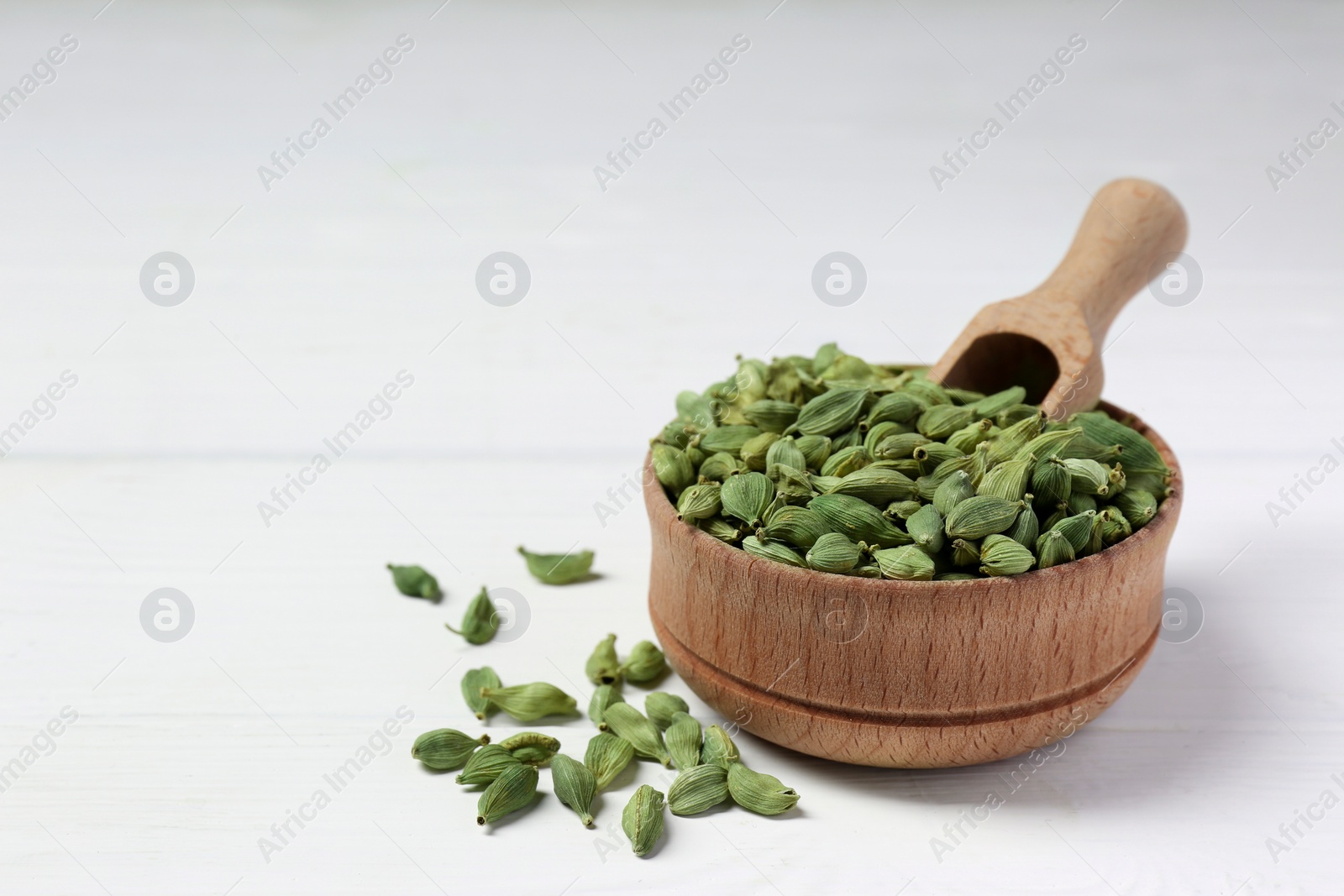 Photo of Bowl and scoop with dry cardamom on white table. Space for text