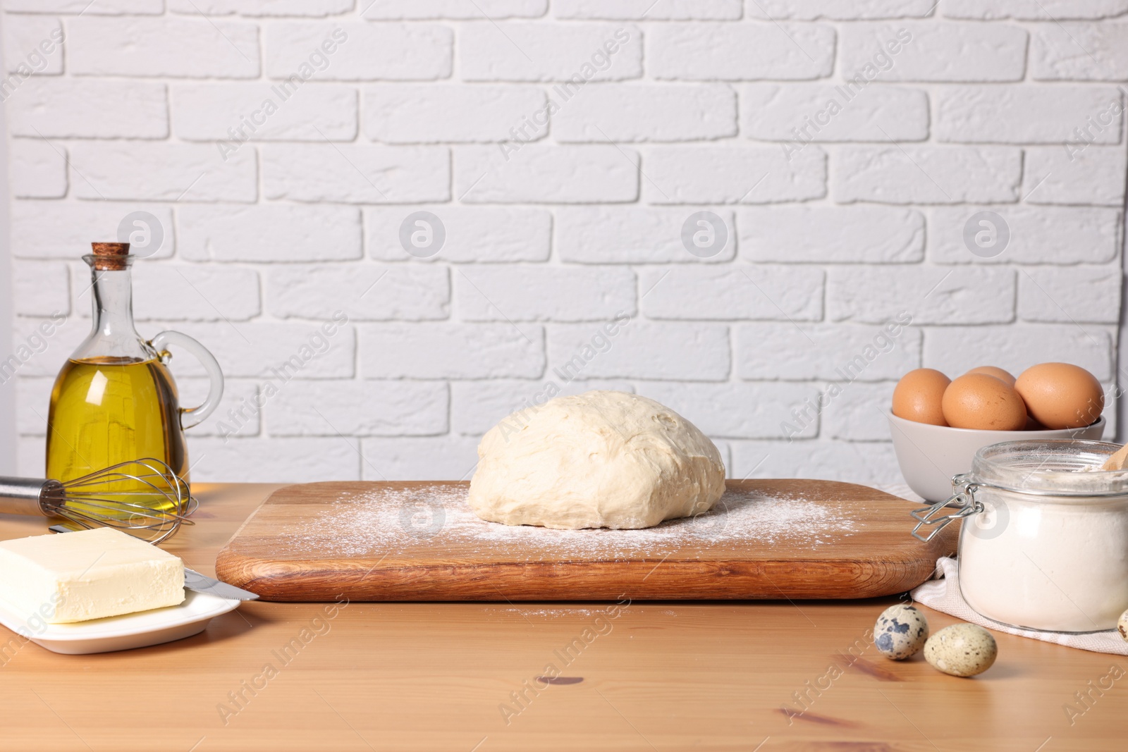 Photo of Fresh dough sprinkled with flour and other ingredients on wooden table near white brick wall