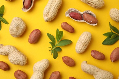 Photo of Fresh peanuts and leaves on yellow table, flat lay