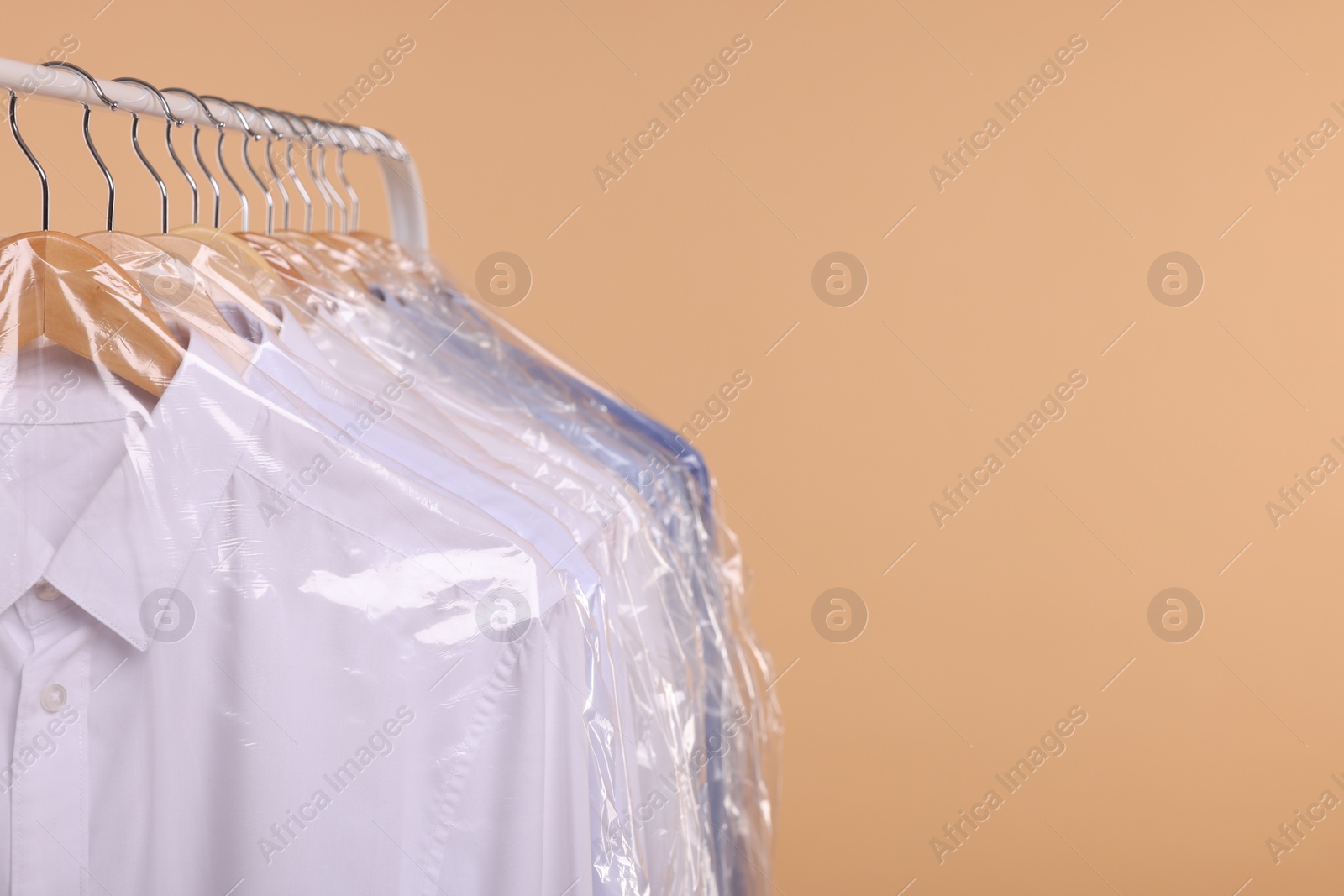 Photo of Dry-cleaning service. Many different clothes in plastic bags hanging on rack against beige background, closeup and space for text