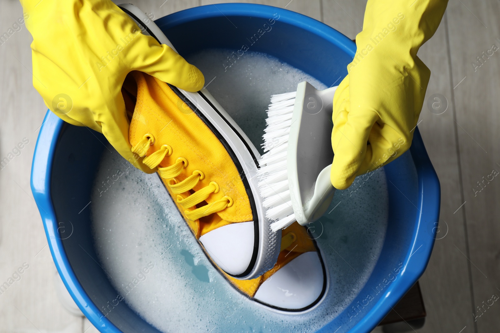 Photo of Woman with gloves and brush cleaning stylish sneakers in wash basin, top view