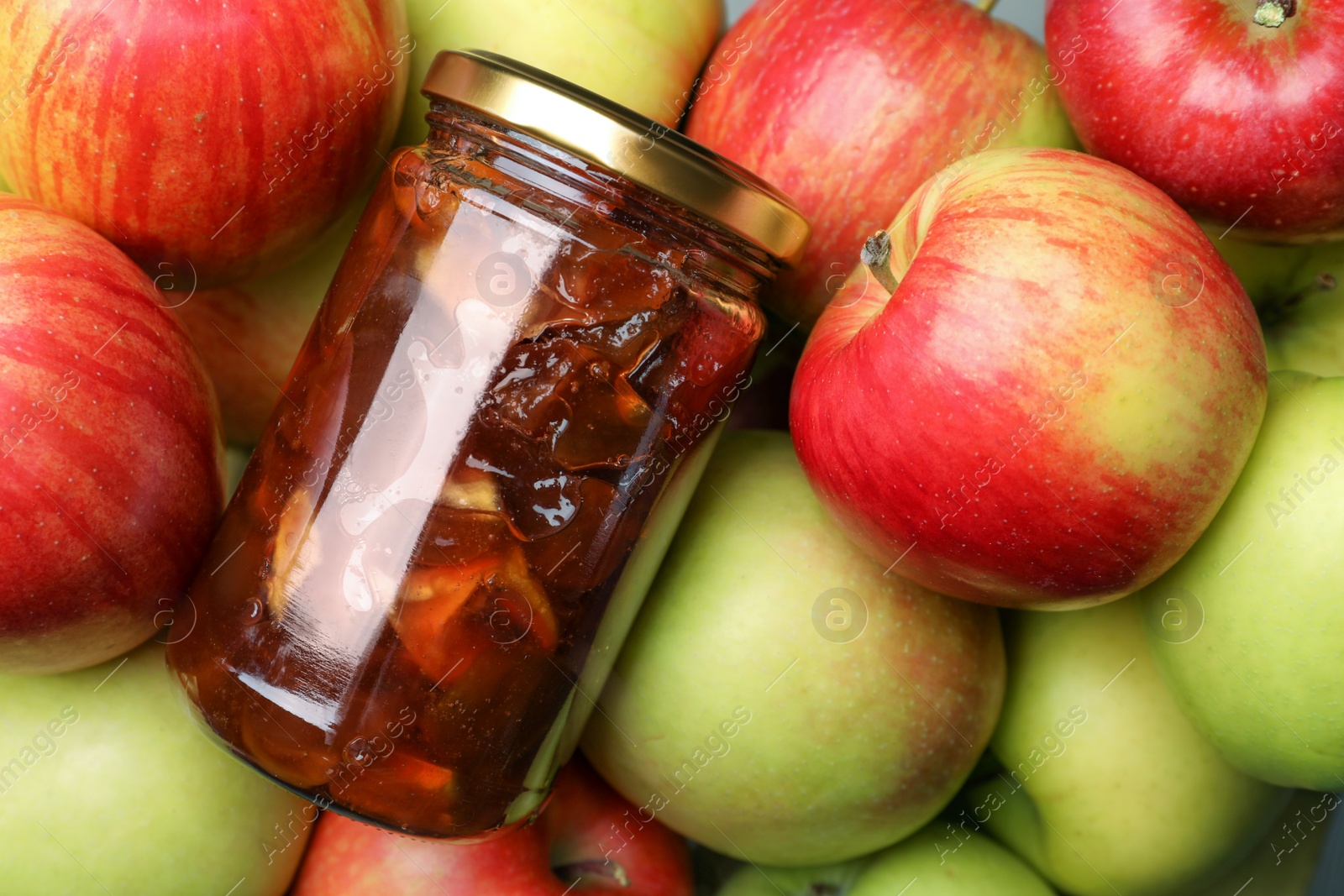 Photo of Delicious apple jam in jar on fresh fruits, top view