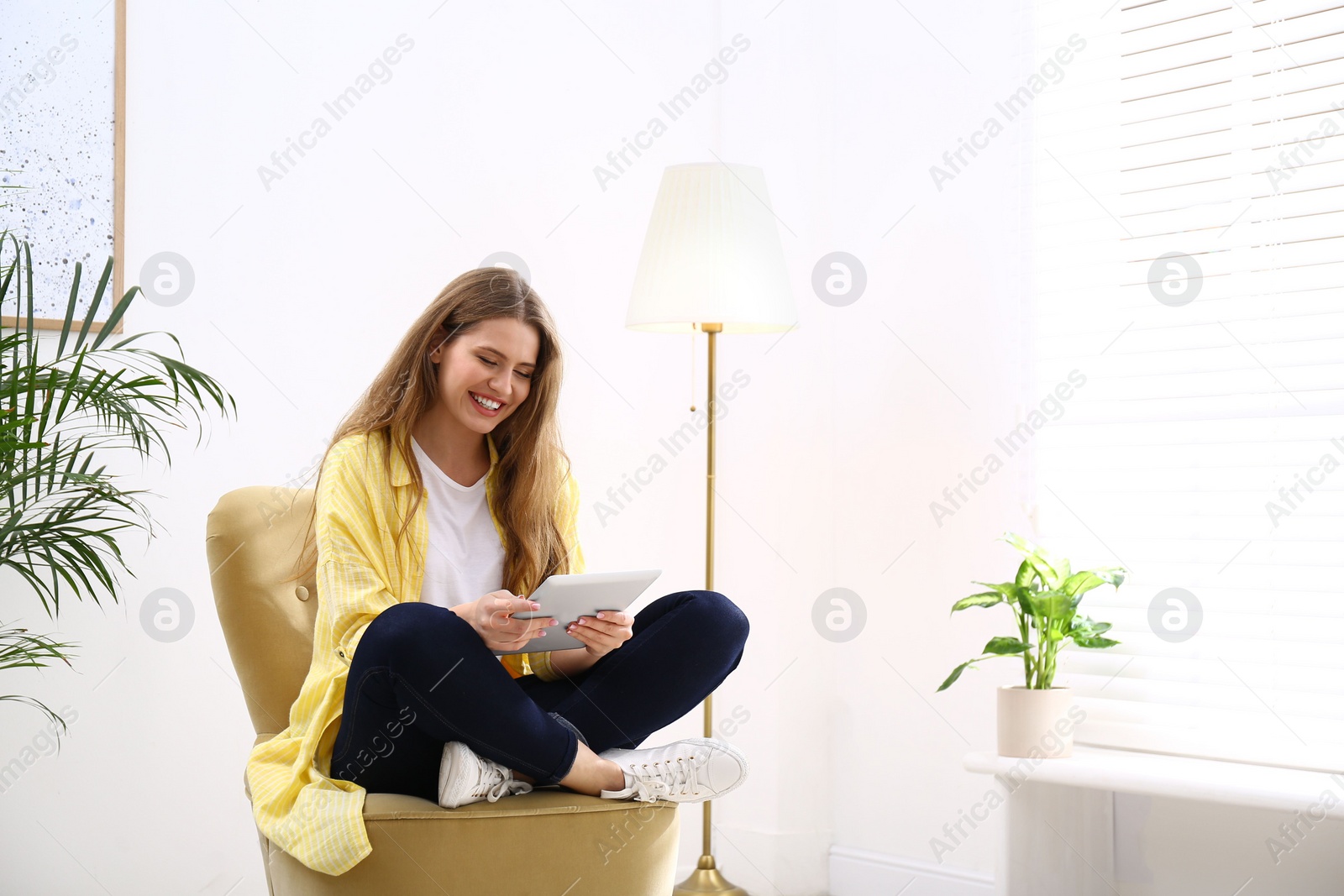 Photo of Young woman with tablet resting in armchair at home. Space for text