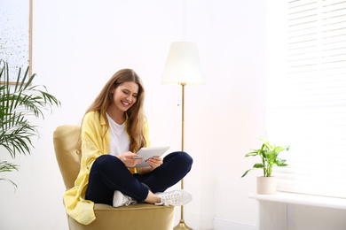 Photo of Young woman with tablet resting in armchair at home. Space for text