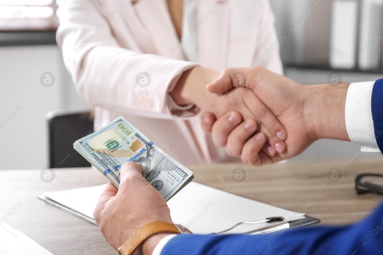 Photo of Man shaking hands with woman and offering bribe at table, closeup