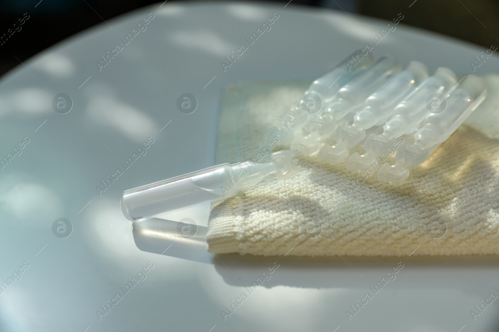 Photo of Single dose ampoules of sterile isotonic sea water solution and towel on white table, closeup