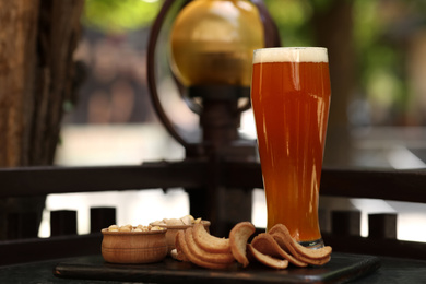 Photo of Glass of tasty beer served with snacks on table outdoors, space for text