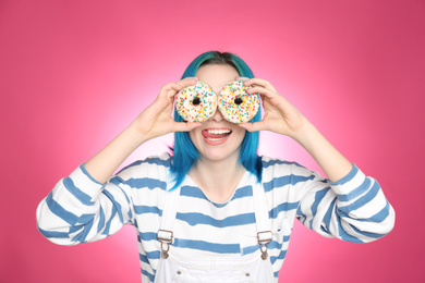Photo of Young woman with bright dyed hair holding donuts on pink background