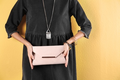 Young woman in stylish outfit with purse on color background, closeup