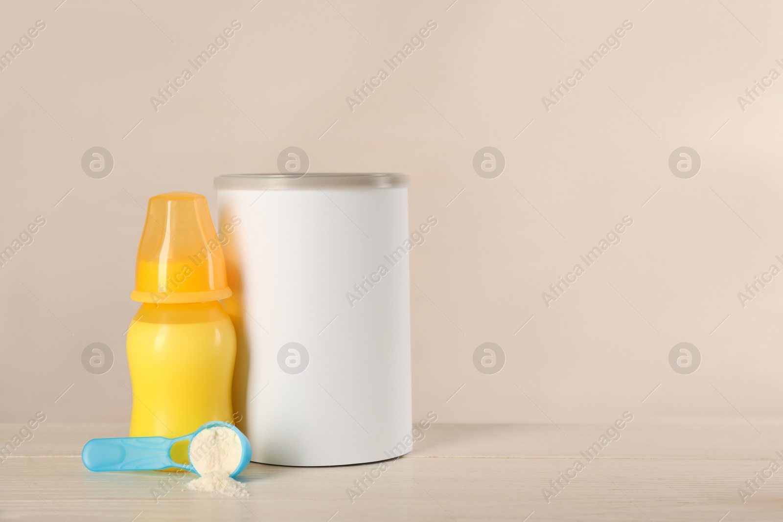 Photo of Blank can of powdered infant formula, feeding bottle and scoop on white wooden table, space for text