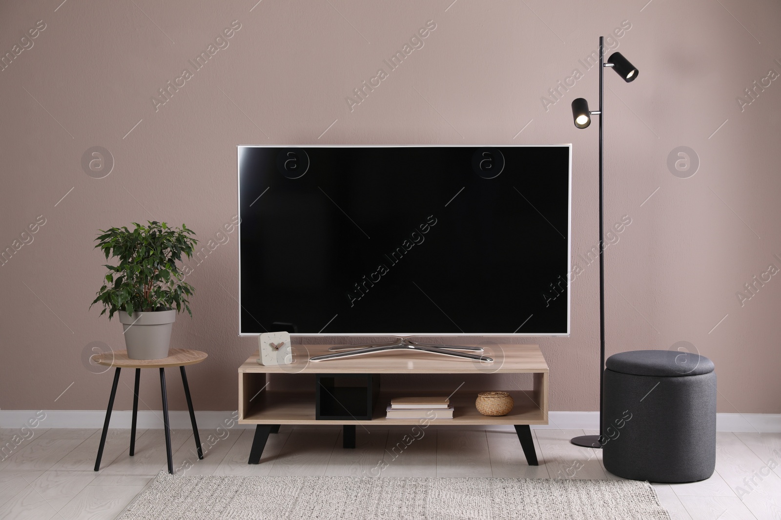 Photo of Modern TV on stand near pale pink wall indoors. Interior design