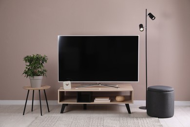 Modern TV on stand near pale pink wall indoors. Interior design