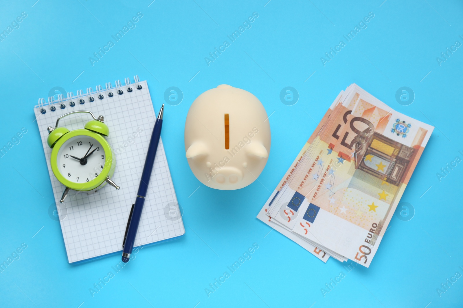 Photo of Piggy bank, alarm clock, notebook and banknotes on light blue background, flat lay