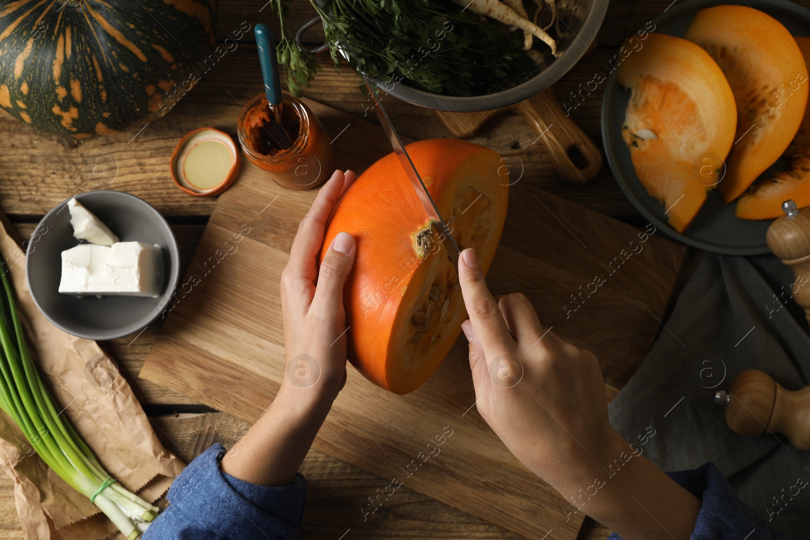 Photo of Woman cutting fresh ripe pumpkin at wooden table, top view