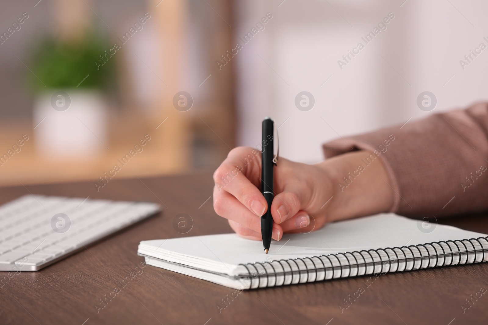 Photo of Woman writing in notebook at wooden table indoors, closeup. Space for text