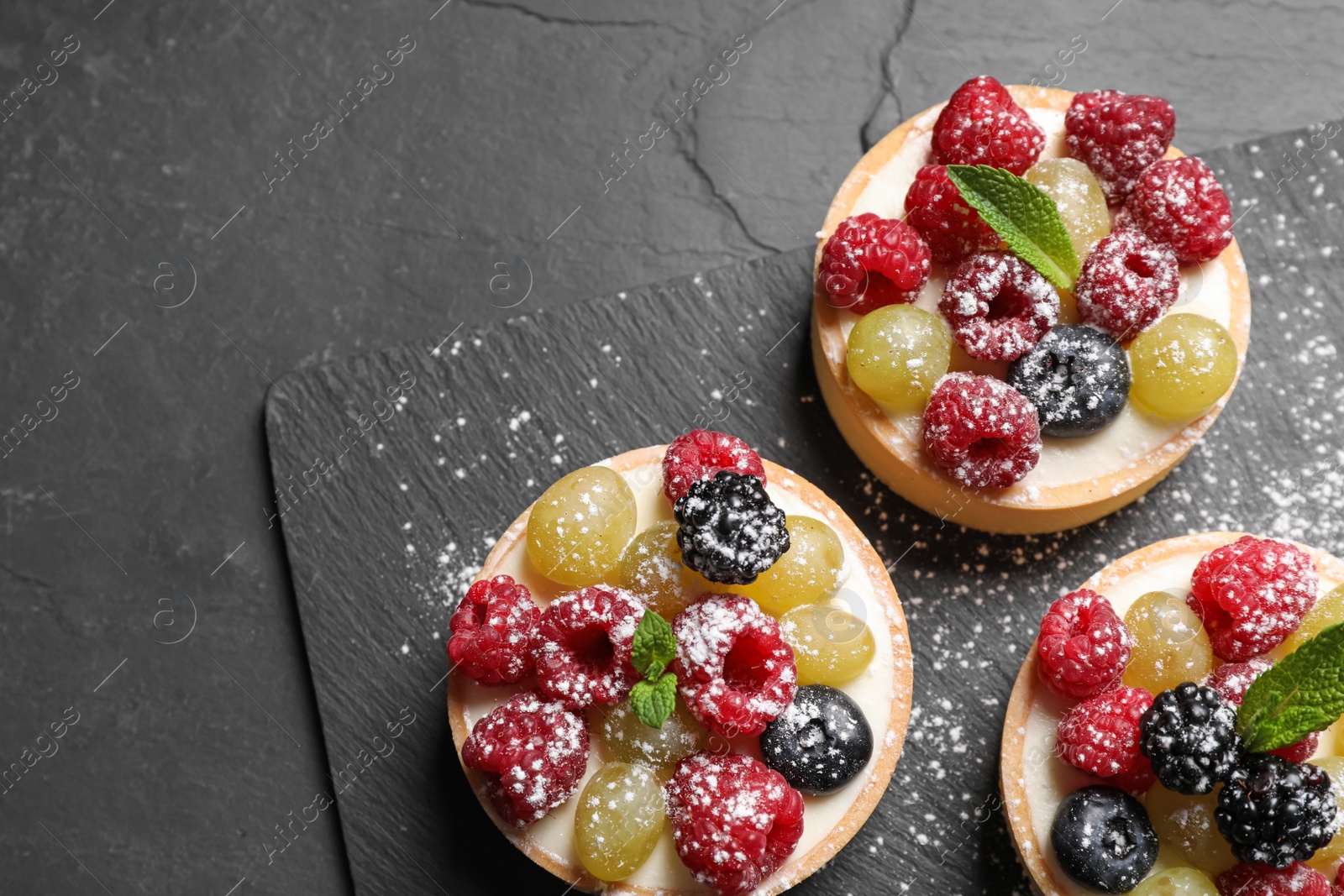 Photo of Delicious tartlets with berries on black table, top view