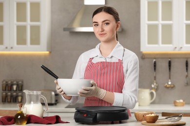 Young woman cooking delicious crepes in kitchen