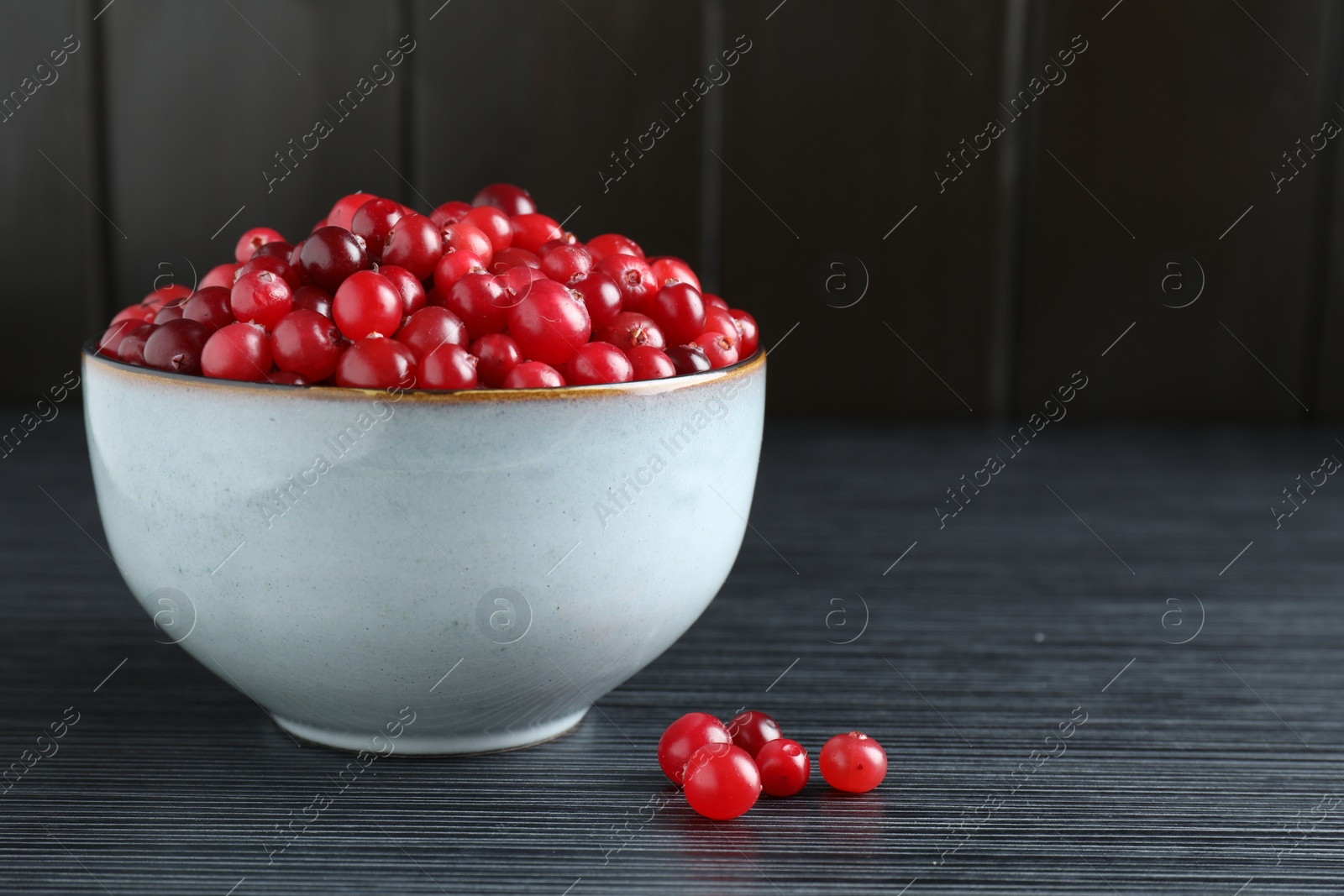 Photo of Cranberries in bowl on black wooden table, closeup. Space for text