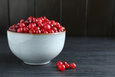 Photo of Cranberries in bowl on black wooden table, closeup. Space for text