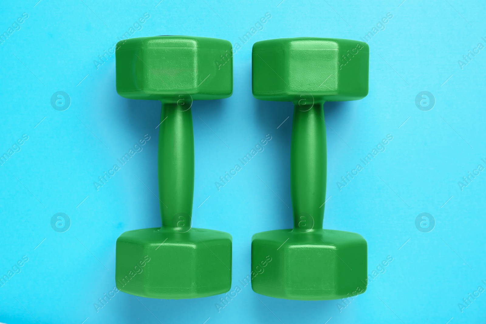 Photo of Green dumbbells on light blue background, flat lay