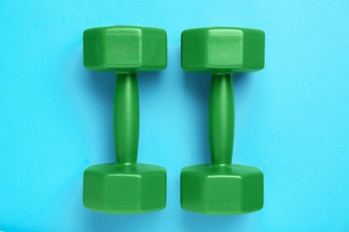 Green dumbbells on light blue background, flat lay