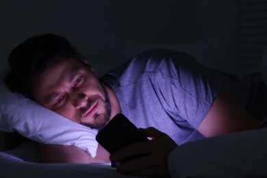 Photo of Man using smartphone in bed at night. Internet addiction