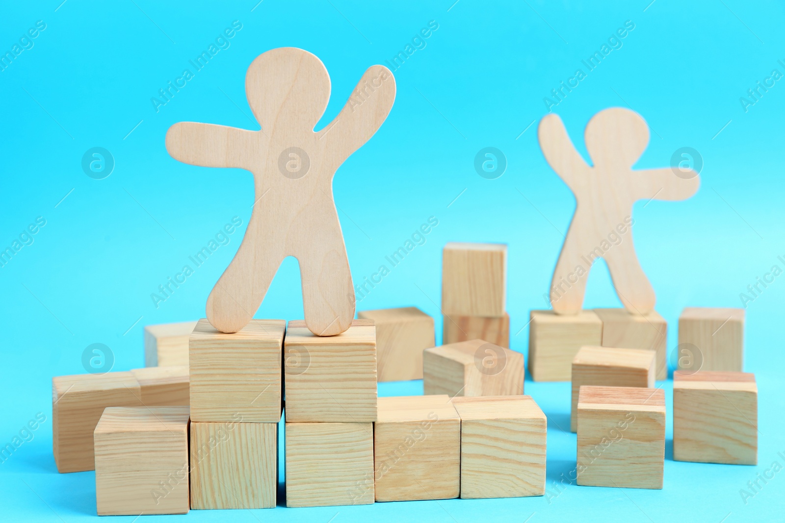 Photo of Wooden cubes and human figures on light blue background. Social roles concept