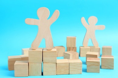 Photo of Wooden cubes and human figures on light blue background. Social roles concept