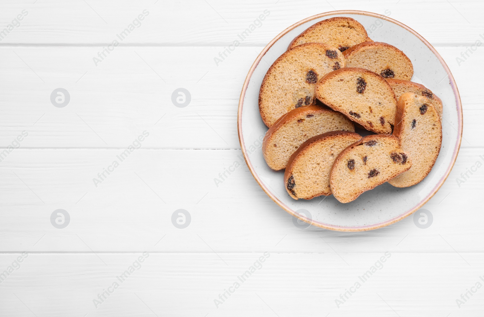 Photo of Plate of sweet hard chuck crackers with raisins on white wooden table, top view. Space for text