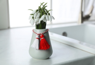 Photo of Beautiful snowdrops with traditional martisor on table indoors, space for text. Symbol of first spring day