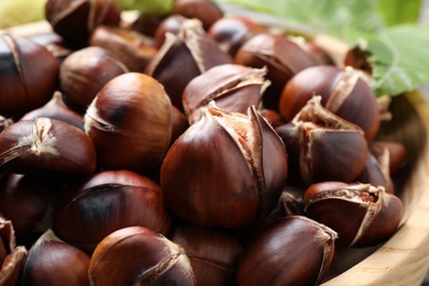 Photo of Delicious roasted edible chestnuts in wooden bowl, closeup