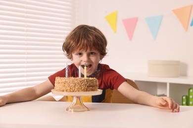 Cute boy with birthday cake at table indoors