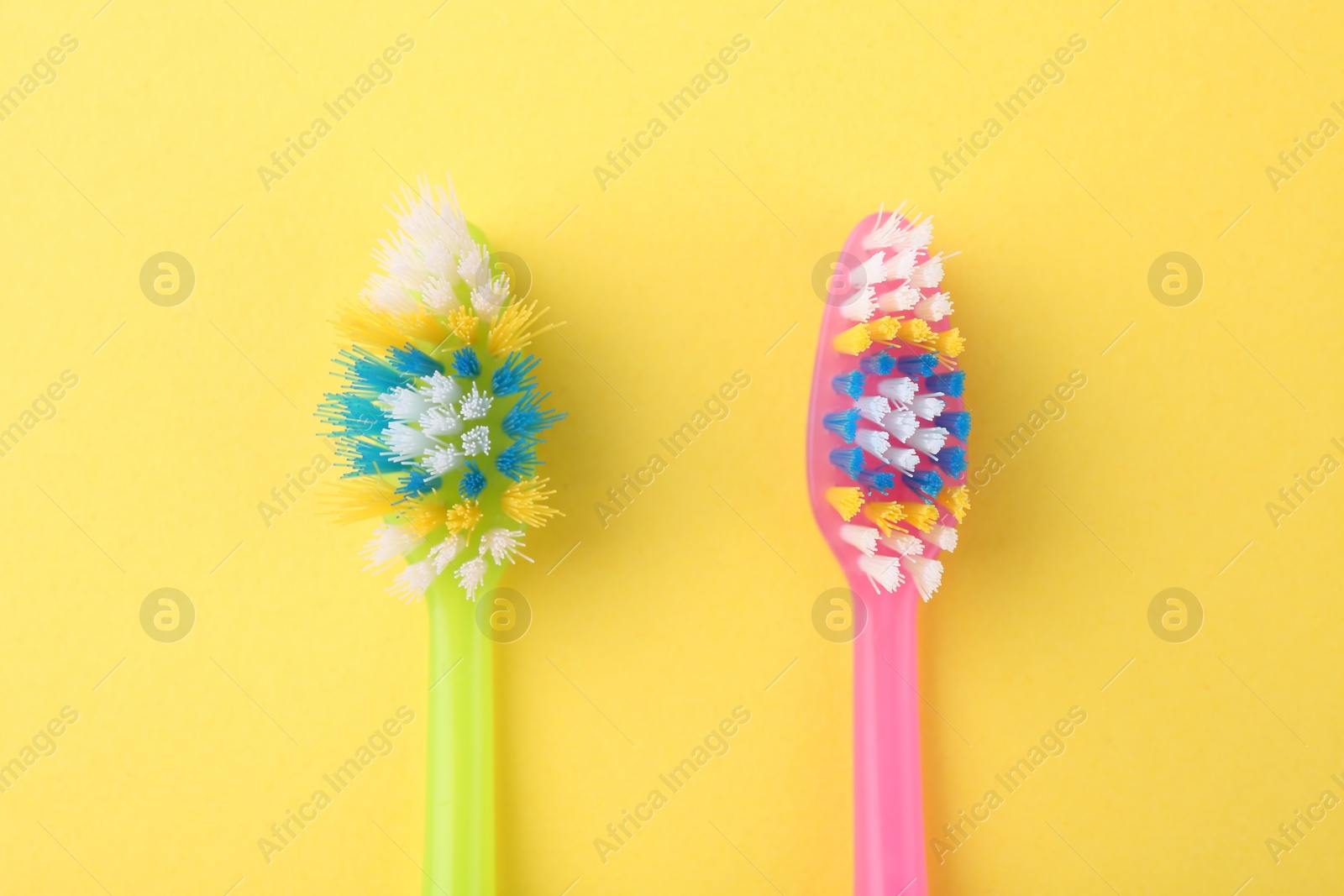 Photo of Colorful plastic toothbrushes on yellow background, flat lay